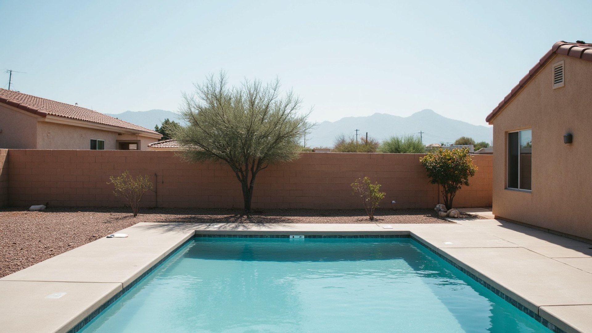 Backyard pool behind a tan stucco Avondale home with a tile roof, block wall and gravel desert landscaping