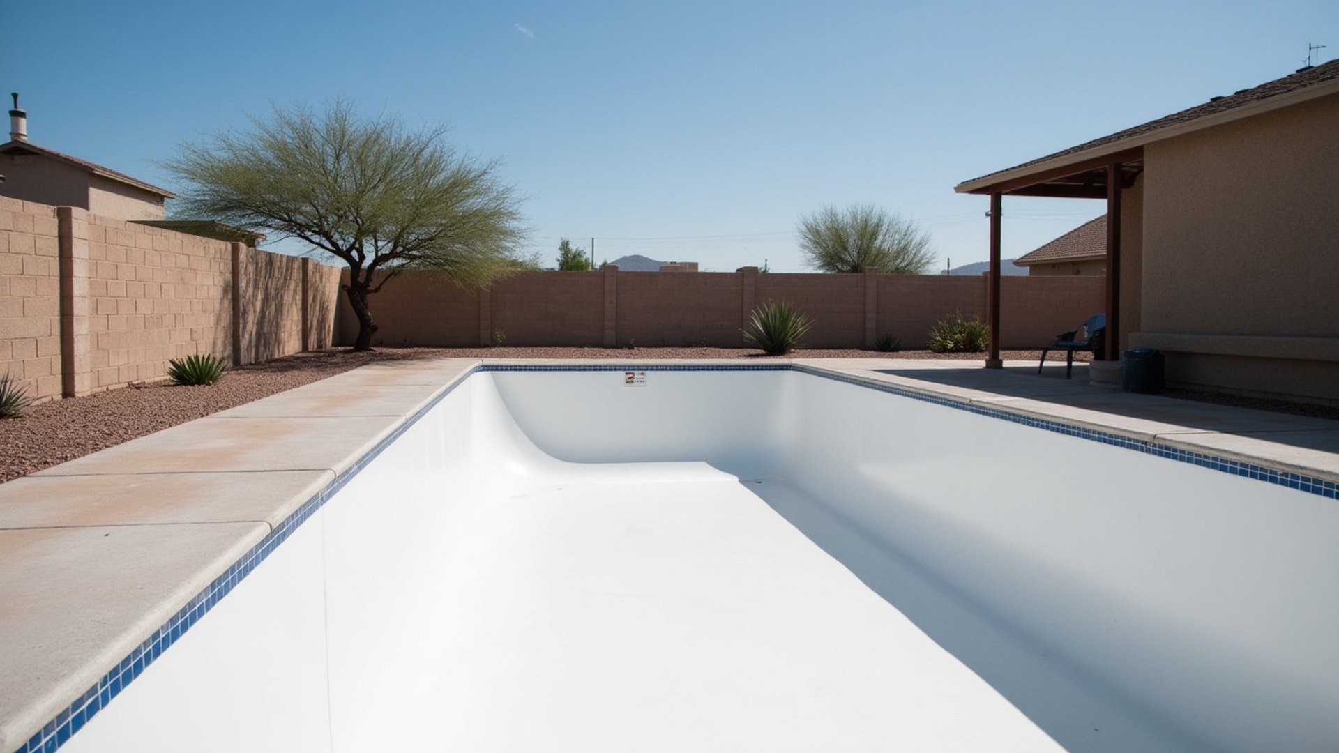 Drained backyard pool with a freshly troweled smooth white interior, stucco house and desert landscaping behind